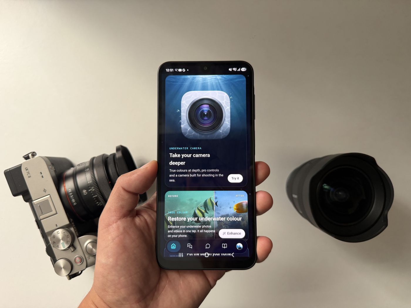 An Android phone showing Diving Standard's camera screen, held between a mirrorless camera and a wide-angle lens
