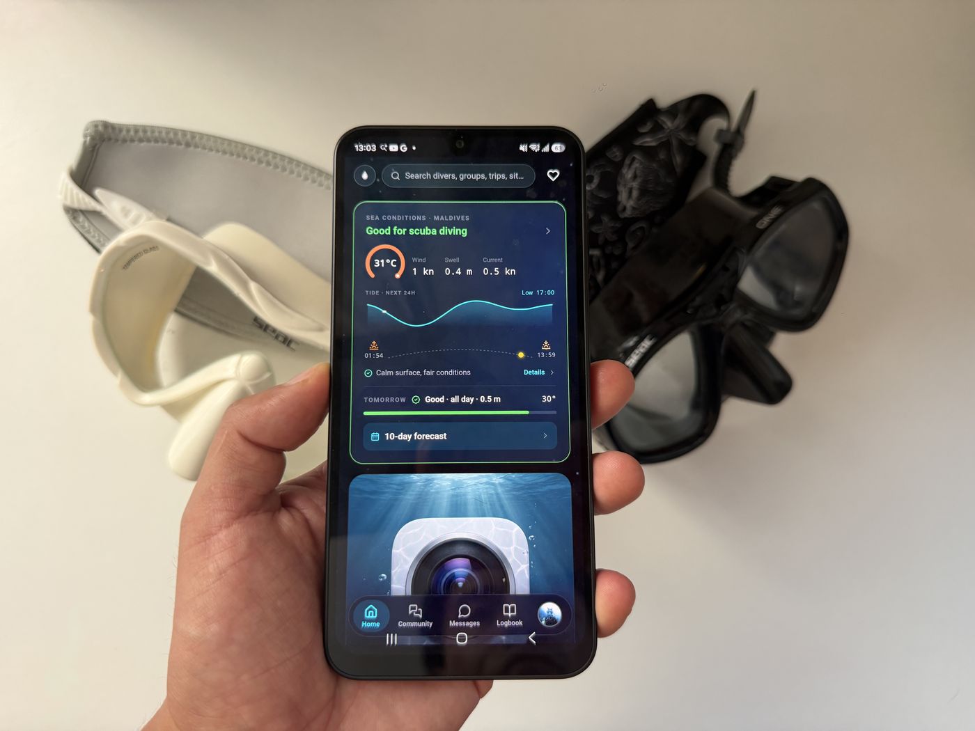 An Android phone showing Diving Standard's home screen held in front of a white snorkel mask and a black mask