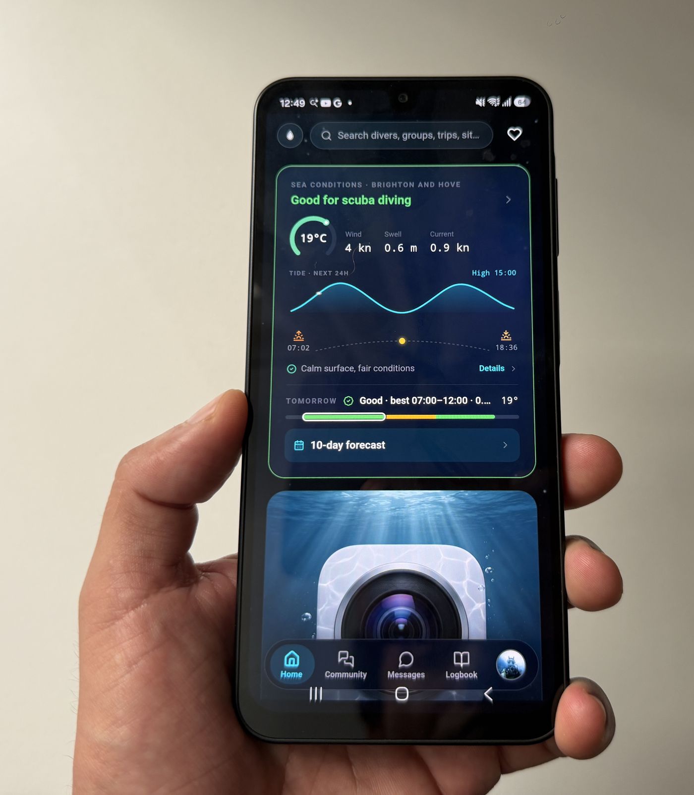 A hand holding an Android phone showing the Diving Standard home screen with a sea conditions card rating the day good for scuba diving