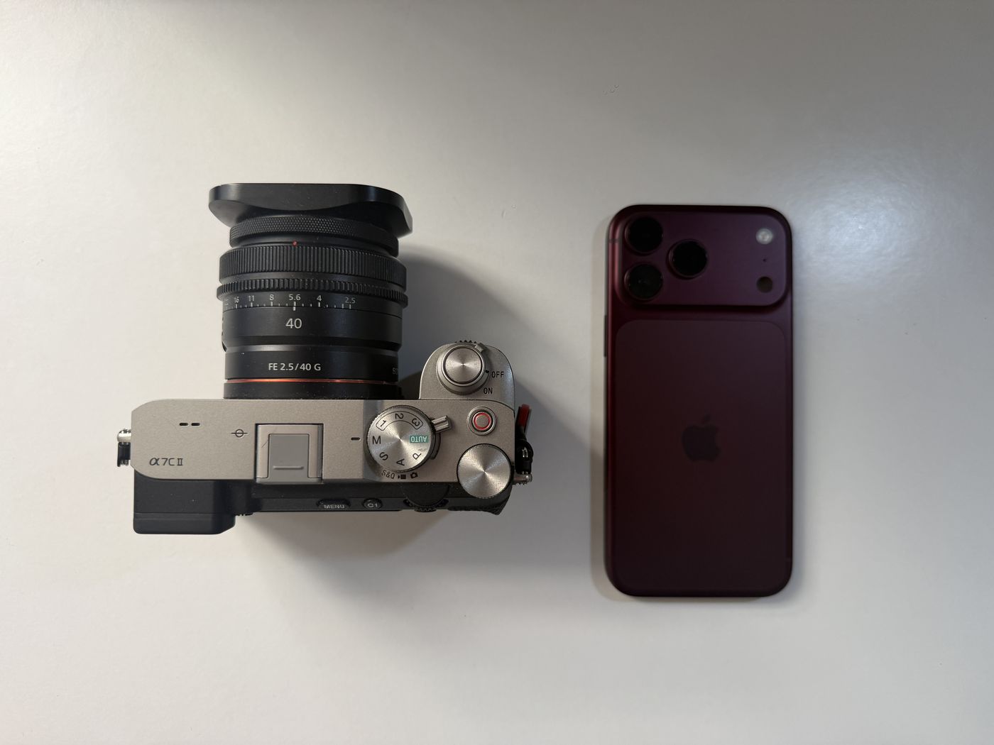 An iPhone 18 Pro Max lying next to a mirrorless camera on a white table
